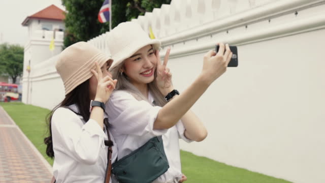 Happy-Asian-lesbian-couples-selfie-video-chat-with-friends-enjoying-traveling-in-Thailand.-Beautiful-young-women-having-fun-in-vacation-time.-LGBT-concept.
