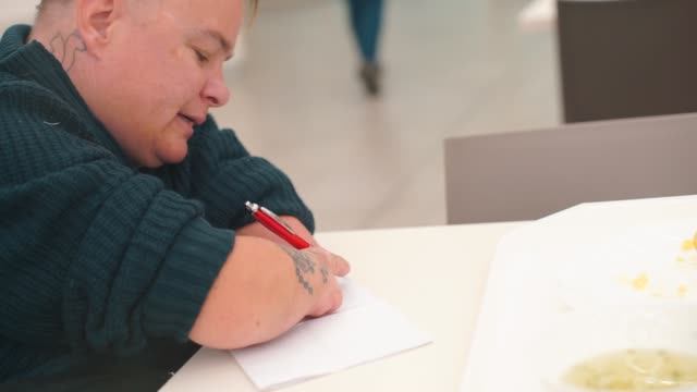Behinderte-Frau-schreibt-Stifttext-auf-Papier-am-Tisch