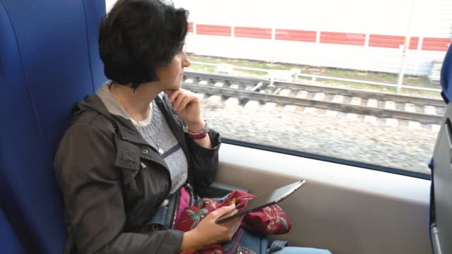 kaukasische-Frau-sitzt-Zug-Fenster-hält-Tablet-schaut-aus-Fenster-Requisiten-ihr-Kinn