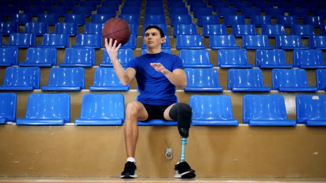 A-male-with-an-artificial-leg-is-playing-with-a-basket-ball-while-sitting