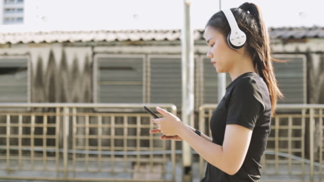 Beautiful-female-athlete-running-wearing-headphones-using-a-smartphone-listening-to-music-while-walking-in-the-urban-city.-Jogging-lifestyle-healthy.