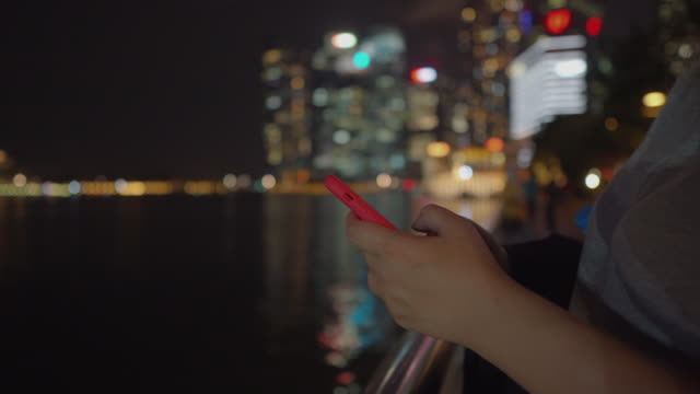 woman-using-smartphone-at-night-time-on-embankment