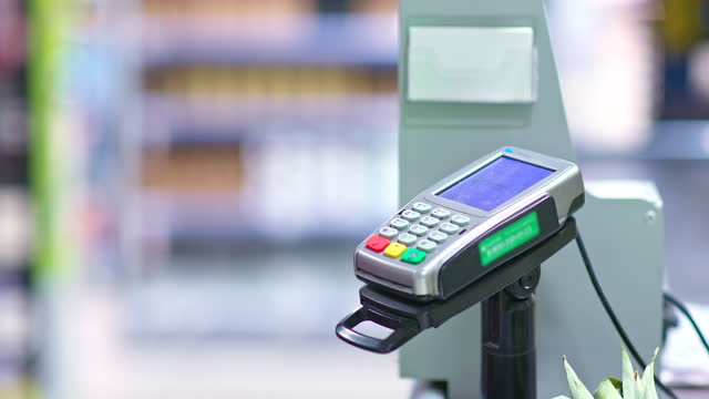 Close-up,-payment-terminal-in-a-supermarket,-contactless-payment-for-purchases,-nfc.-Woman's-hand-brings-the-phone-to-the-terminate-for-payment.-4k,-ProRes