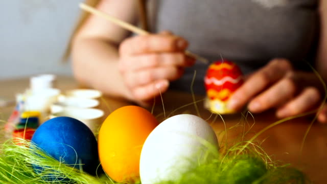 Eine-junge-Frau-malt-Easter-Egg-mit-einem-Pinsel-auf-dem-Hintergrund-der-Holztisch