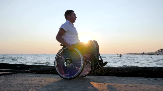 disabled-person-sitting-in-wheelchair-on-embankment,-cheerful-disabled-man-pushing-himself-in-wheelchair