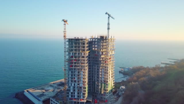Aerial-city-view.-Construction-of-a-high-rise-skyscraper-on-the-ocean-by-two-cranes.-The-camera-is-moving-at-maximum-speed.-After-turning-to-the-right