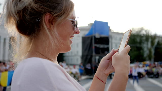 lächelnde-Frau-in-Sonnenbrille-schreibt-Nachricht-auf-Handy-stehen-im-Zentrum