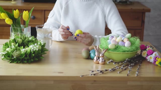 Frau-malt-ein-gelbes-Ei-auf-dem-Tisch-mit-Osterschmuck
