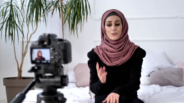 Young-beautiful-indian-girl-in-hijab-blogger-talking-on-camera,-counts,-outraged,-gesturing,-white-room,-home-comfort-in-background.-Close-up-50-fps