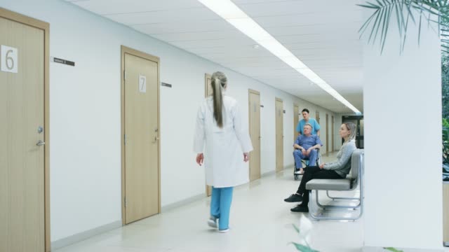 En-el-pasillo-del-Hospital,-la-enfermera-empuja-Senior-hombre-en-silla-de-ruedas,-pacientes-esperan-a-su-médico,-personal-profesional-ocupado-caminar.-Limpio,-nuevo-Hospital-con-personal-médico-profesional.