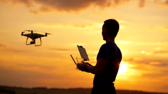 Der-Mann-kontrolliert-Quadrocopter-auf-dem-Sonnenuntergang-Hintergrund