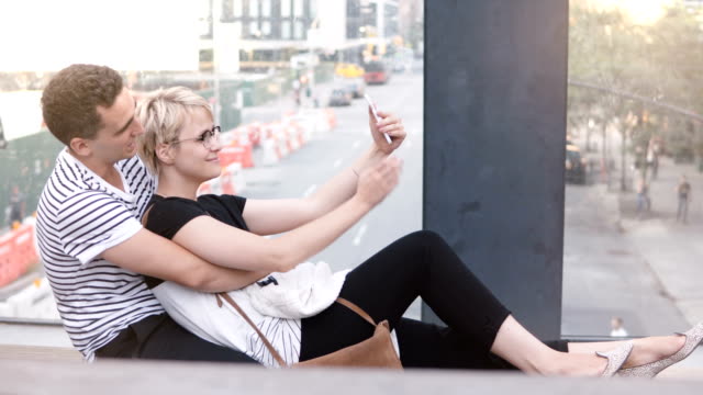 Multiethnische-romantische-Brautpaar-sitzt-auf-einer-New-Yorker-Straße-Brücke,-unter-Smartphone-Selfie-und-Spaß-haben-lächelnd