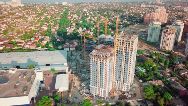 Aerial-drone-shot.-Construction-of-high-rise-buildings-in-the-developing-area-of-a-large-city.-Sunset-shot.-In-the-frame-moving-and-working-construction-cranes-and-many-houses-under-construction.-wide-shot