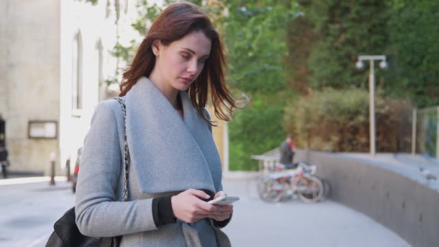 Junge-weiße-Frau-stehen-auf-einer-Straße-in-London-mit-ihrem-Smartphone,-dreht-sich-und-verlässt-schossen-schließen,-Fokus-auf-Vordergrund