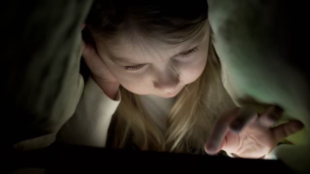 Junge-Mädchen-versteckt-unter-der-Bettdecke-zu-spät-nach-dem-Zubettgehen-digital-Tablet-Gerät-verwenden