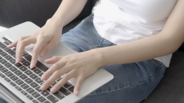 Closeup-hand-of-freelance-woman-working-and-typing-on-laptop-computer-sitting-on-couch-at-living-room,-girl-on-sofa-using-notebook-checking-email-or-social-network,-business-and-lifestyle-concept.