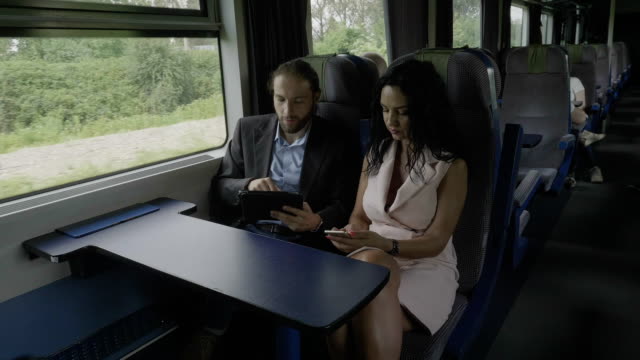 Joven-empresario-hombre-trabajando-en-Tablet-PC-discutiendo-con-empresaria-sentado-en-un-tren-durante-el-viaje-de-negocios