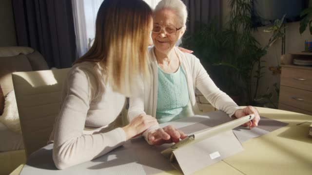 Fröhliche-Frau-und-Großmutter-nutzen-digitale-Tablets-gemeinsam