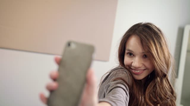 Junge-Frau-macht-Selfie-Foto-auf-Handy-im-Schlafzimmer