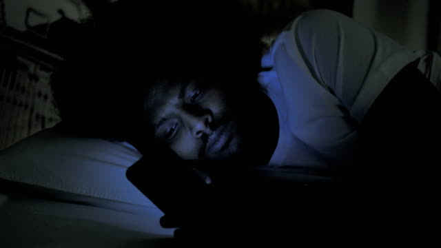 Afrikanischer-Mann-benutzt-Telefon-in-Bett-in-der-Nacht