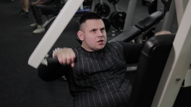 Cheerful-fat-man-performs-a-wrong-exercise-in-the-gym.-For-the-first-time-in-a-fitness-club