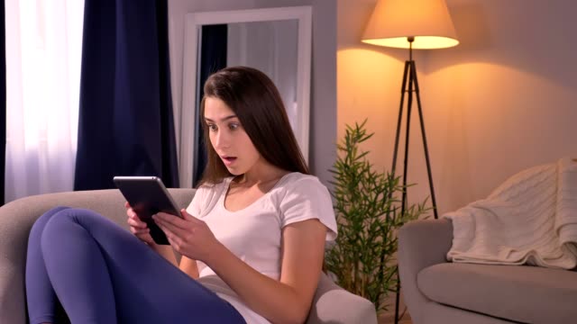 Closeup-portrait-of-young-attractive-caucasian-female-using-the-tablet-and-getting-shocked-looking-at-camera-emotionally