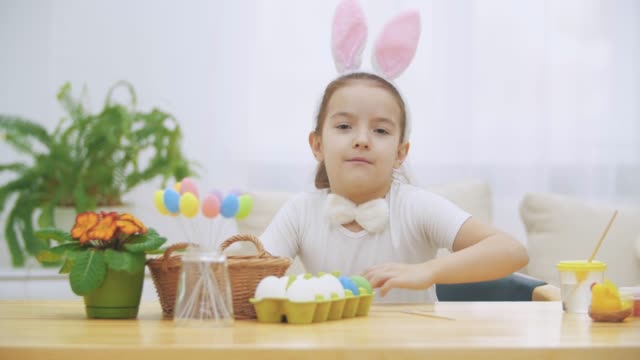 Little-nice-girl-is-climbing-into-a-soft-chair,-and-is-playing-with-bunny.-She-sits-down-at-the-table-with-Easter-decorations-and-is-painting-a-Bunny.