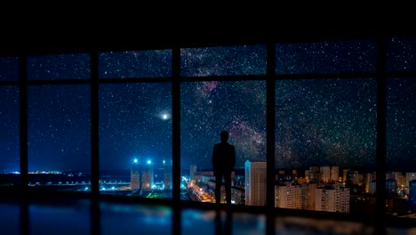 The-man-standing-near-a-window-on-the-city-with-stars-background.-time-lapse