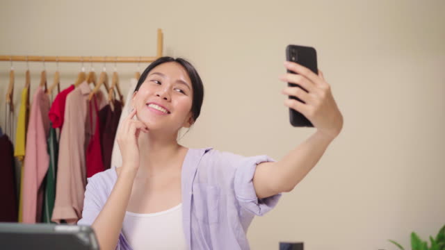 Glücklich-schöne-junge-asiatische-Frau-mit-Smartphone-Selfie-Live-Streaming-online-auf-soziale-Netzwerk.-Beauty-Blogger-präsentieren-Beauty-Kosmetik-sitzen-vor-Tablet-Kamera-für-die-Aufnahme-von-Video.