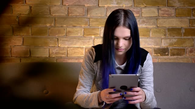 Closeup-shoot-of-young-pretty-caucasian-female-typing-on-the-tablet-while-sitting-on-the-couch-in-a-cozy-apartment-indoors