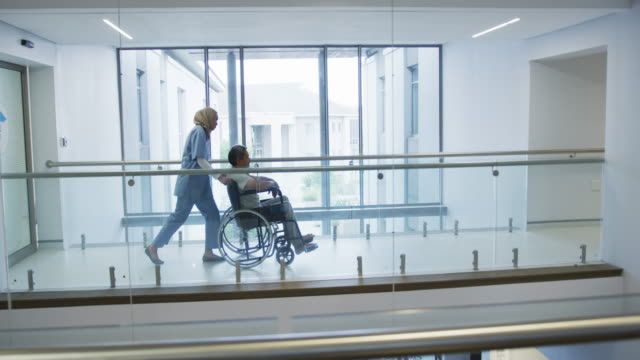 Young-doctor-pushing-patient-in-wheelchair-in-hospital-4k