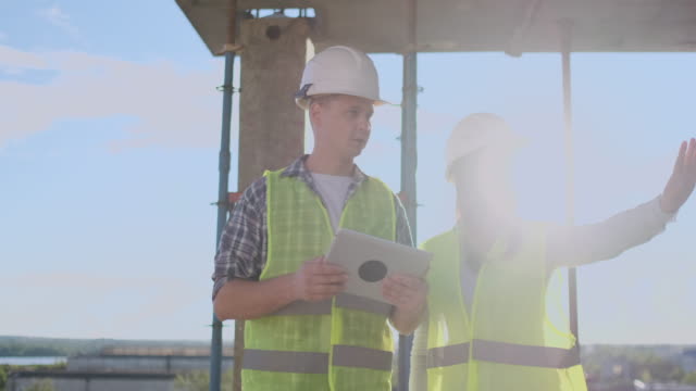 Construction-worker-man-and-architect-woman-in-a-helmet,-discuss-the-plan-of-construction-of-house,-tell-each-other-about-the-design,-holding-a-tablet,-look-at-the-drawings,-background-of-sun-rays