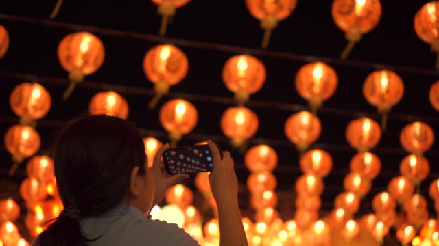 Mujer-asiática-tomar-una-foto-con-teléfono-inteligente.-Hermosas-linternas-de-fondo.-Aún-le-dispararon.