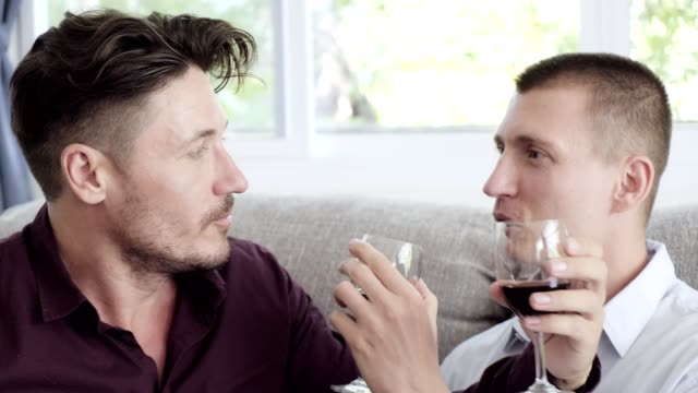 Schwules-Paar-entspannend-auf-der-Couch.-Weinglas-tauschen-und-trinken.