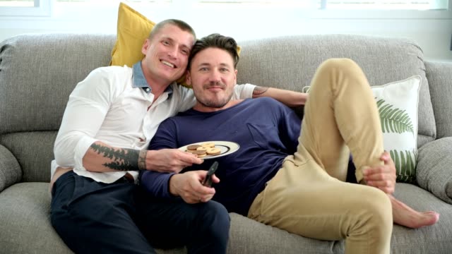 Gay-couple-relaxing-on-couch-watching-tv.-Foot-on-sofa,-very-relax.