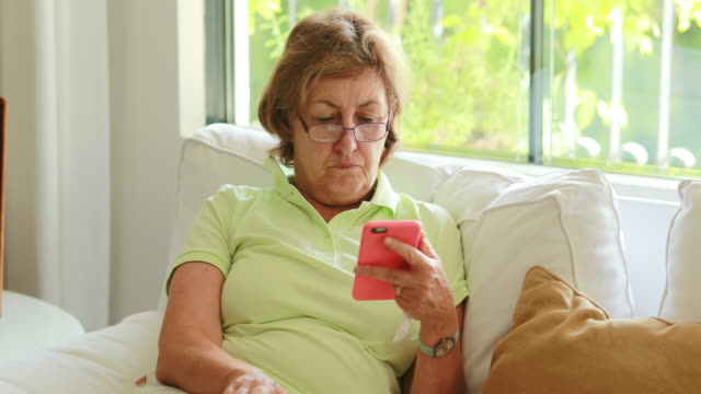 Mujer-mayor-que-sostiene-el-dispositivo-del-teléfono-celular-quitando-los-anteojos-de-lectura-pensando