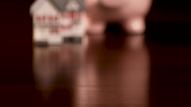 Pan-of-Piggy-Bank-y-Miniature-House-en-superficie-de-madera-oscura