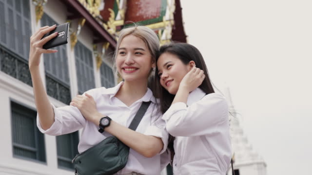 Lächelnde-asiatische-lesbische-Paar-mit-Smartphones-machen-Selfies-ein-Foto.-Schöne-asiatische-Frauen-reisen-mit-einem-Freund-Urlaub-Lebensstil.