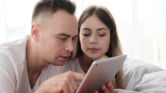 Couple-using-digital-tablet-in-bed