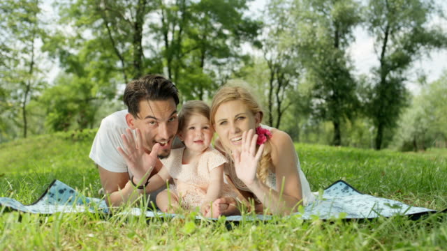 CLOSE-UP:-Perfect-young-happy-family-with-cheerful-beautiful-baby-girl-waving