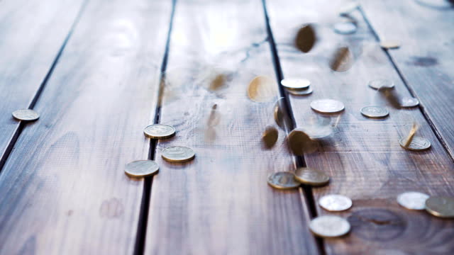 Haufen-von-Münzen-fallen-auf-dem-Holztisch