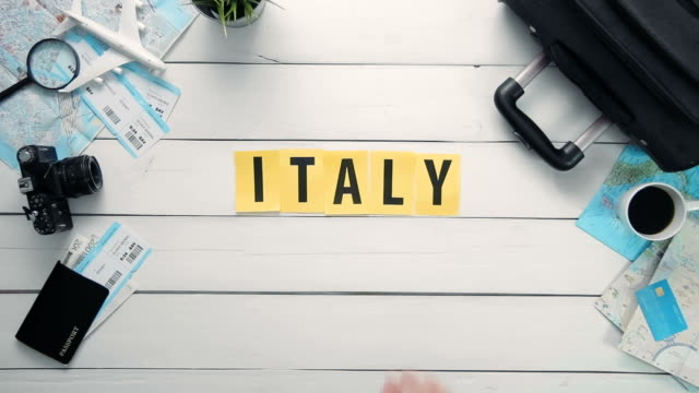Draufsicht-Zeitraffer-Hände-auflegen-weißen-Schreibtisch-Wort-"Italien"-mit-Reisen-Gegenständen-dekoriert