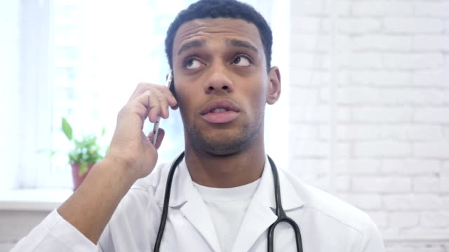 African-American-Arzt-sprechen-auf-Smartphone-im-Krankenhaus