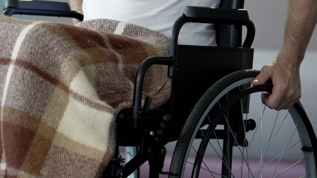 Mann-im-Rollstuhl-zu-schieben-es-durch-die-Hände-nach-der-Verletzung-Rehabilitation-Kurs-ab