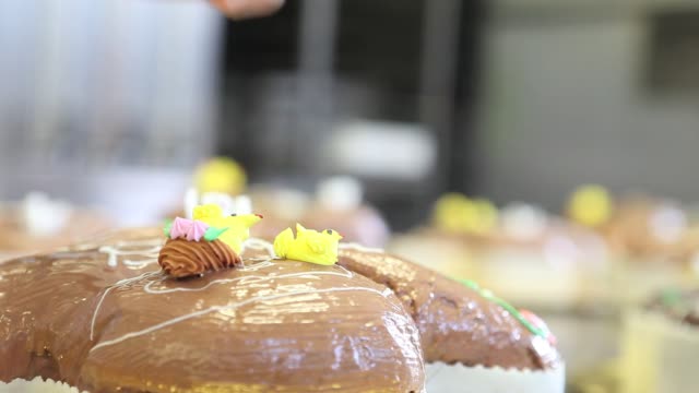 pastry-chef-hands-garnish-Easter-sweet-bread-cakes-with-flowers-fondants-sugar-paste,-closeup-on-the-worktop-in-confectionery