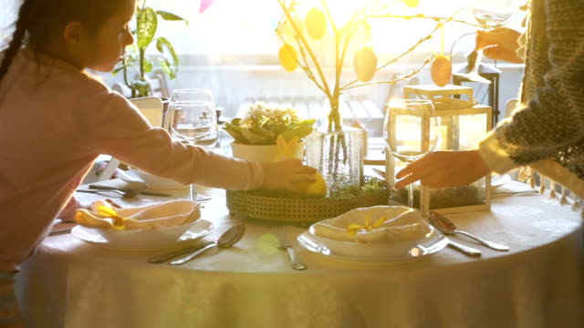 Mujer-y-su-hijita-están-estableciendo-mesa-festiva-de-Pascua-con-conejito-y-huevos-la-decoración