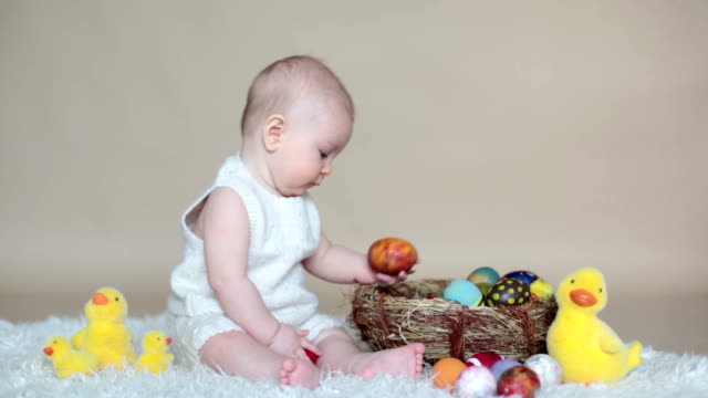 Cute-little-toddler-baby-boy,-playing-with-colorful-easter-eggs-and-little-decorative-ducks,-isolated-shot,-beige-background