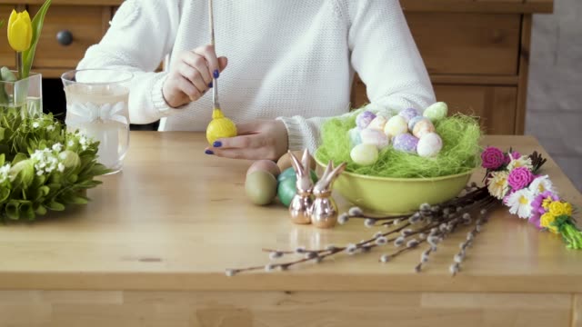 mujer-pinta-un-huevo-amarillo-en-la-mesa-con-decoraciones-de-Pascua