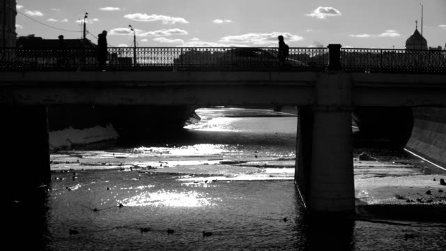 video-blanco-y-negro-con-siluetas-de-personas-caminando-por-el-terraplén-y-el-puente-de-un-río