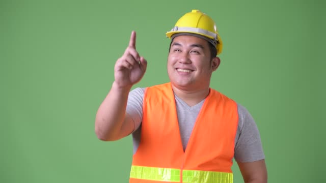Young-handsome-overweight-Asian-man-construction-worker-against-green-background